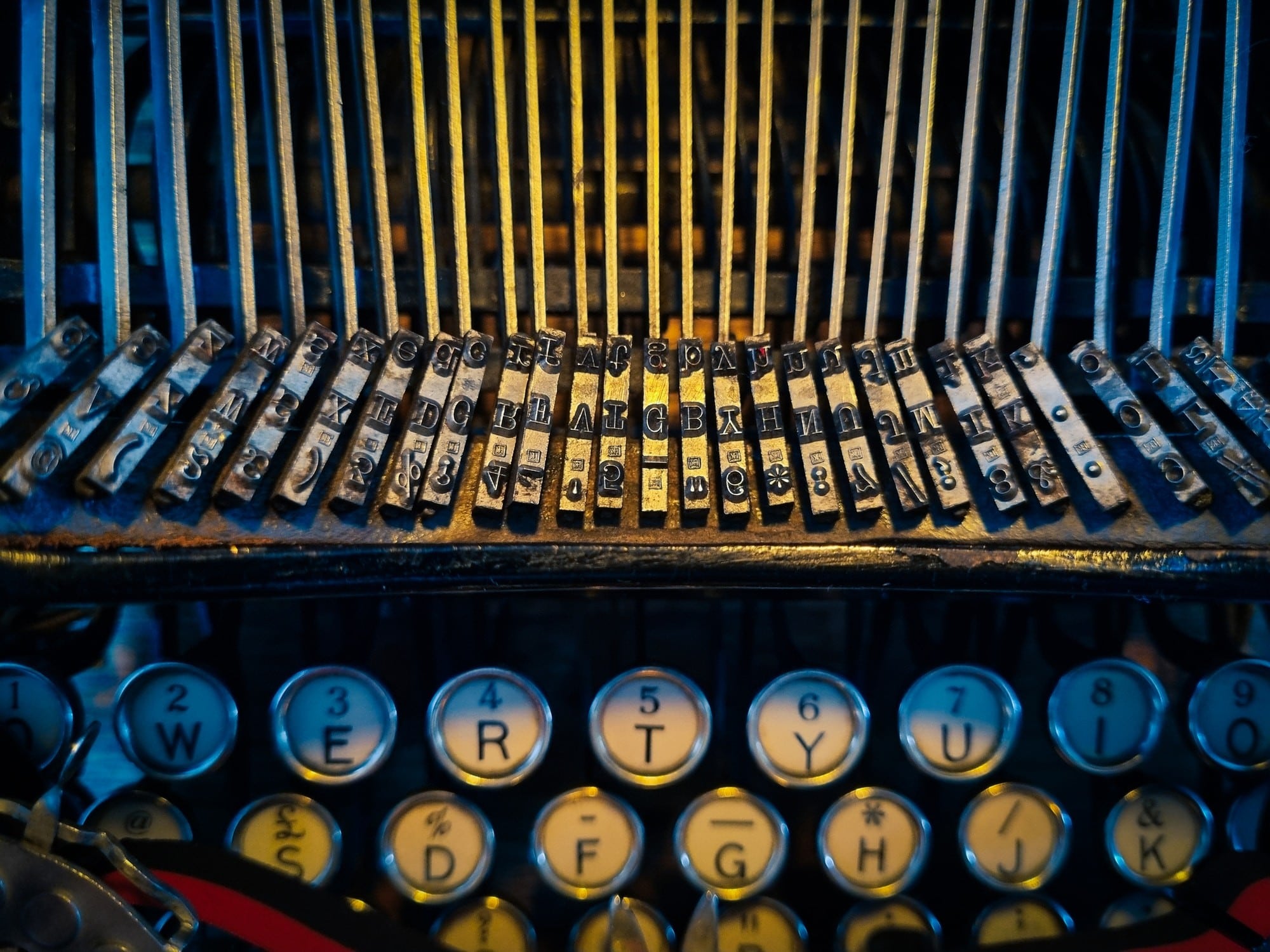 Closeup photo of antique typewriter showing round letter keys and type bar strikers with heavy-contrast lighting shining in center.