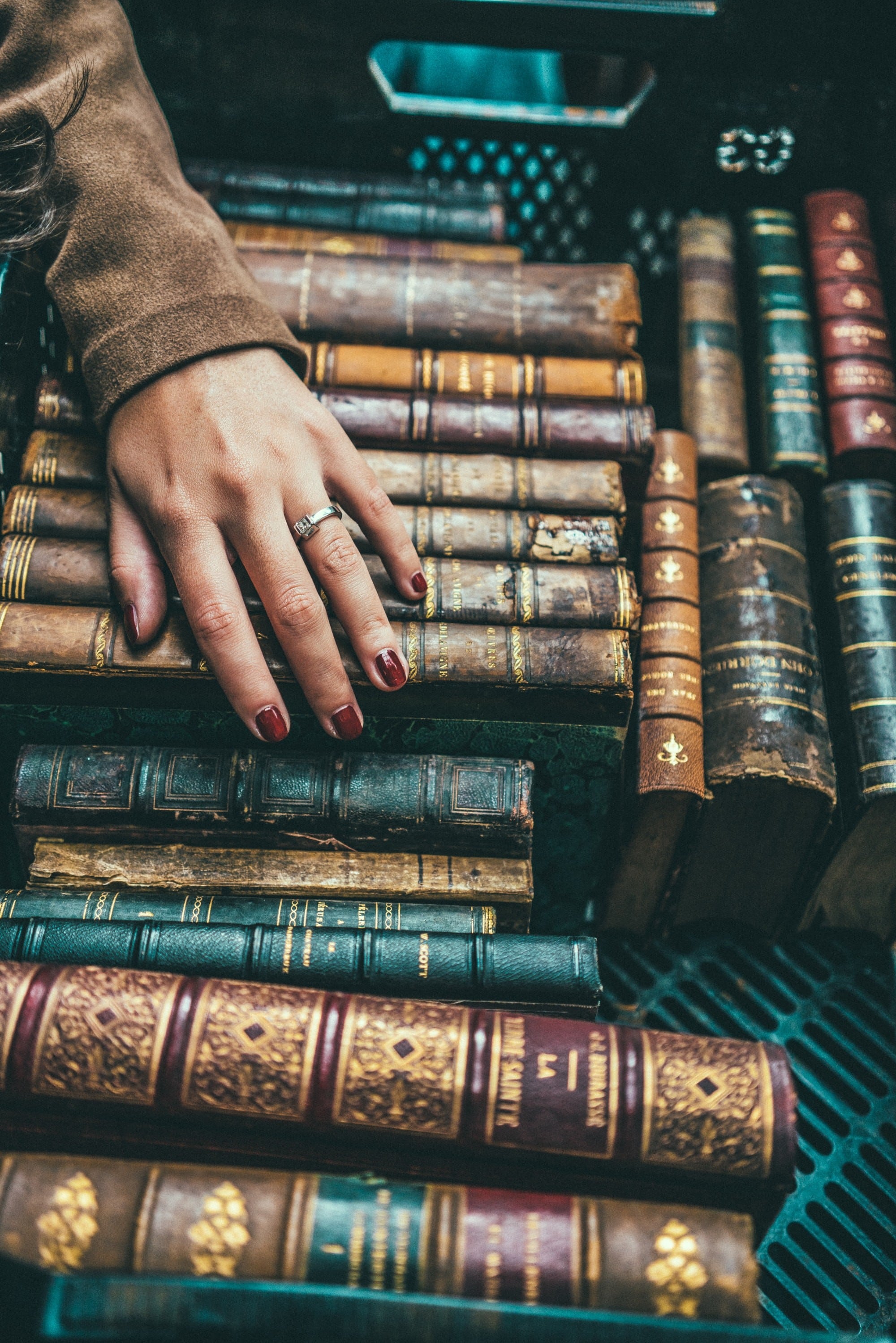 A large spread of antique leather, gold-gilded books with a woman's hand resting on them.